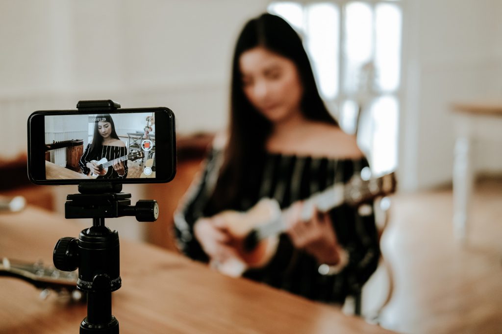 Jeune femme s'enregistrant grâce à son téléphone en jouant de la guitare - Apprendre à s'enregistrer